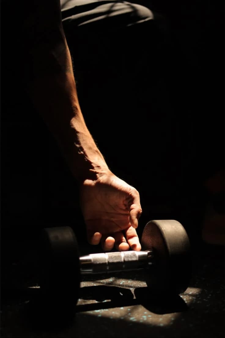Close-up of an athlete reaching for a dumbbell in a gym